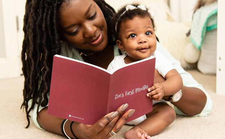 A woman and her baby looking at an open Buzz Book, the cover of the book says Zoe's First Months.
