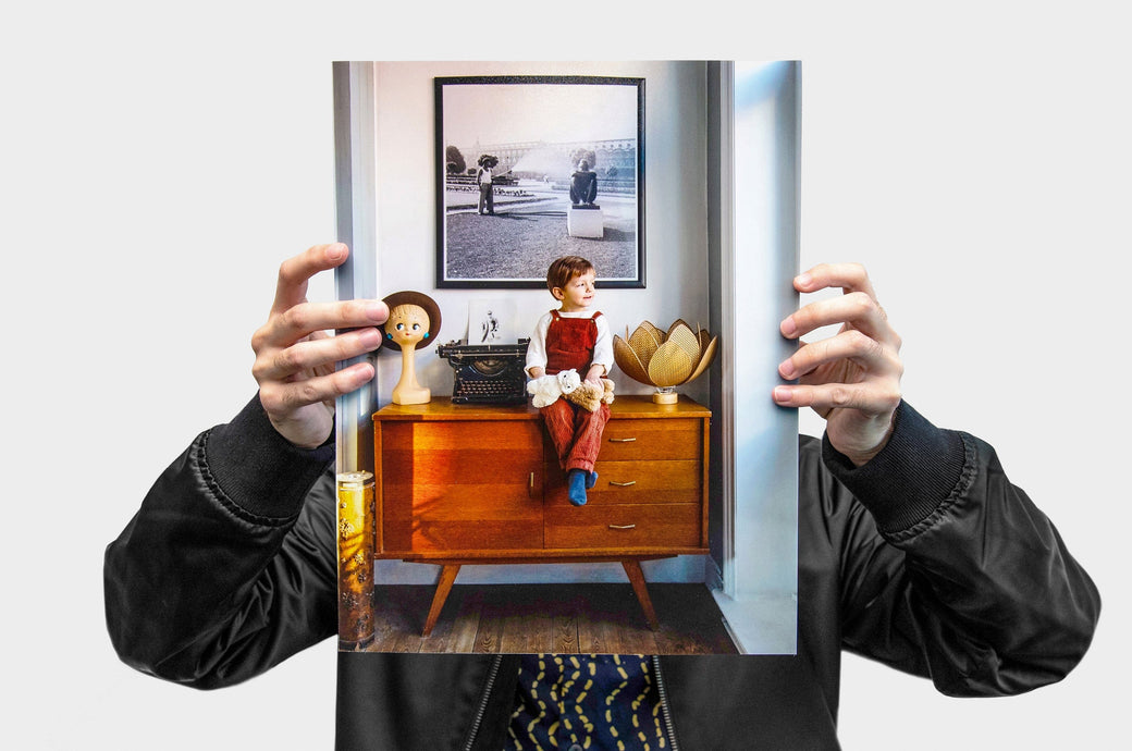 A man holding a 11x14" Portrait Lustre Photo Print featuring a picture of a child sitting on a dresser. 
