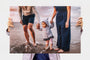 Woman holding a 20x30" Photo Print featuring a picture of a toddler with her parents at the beach. 