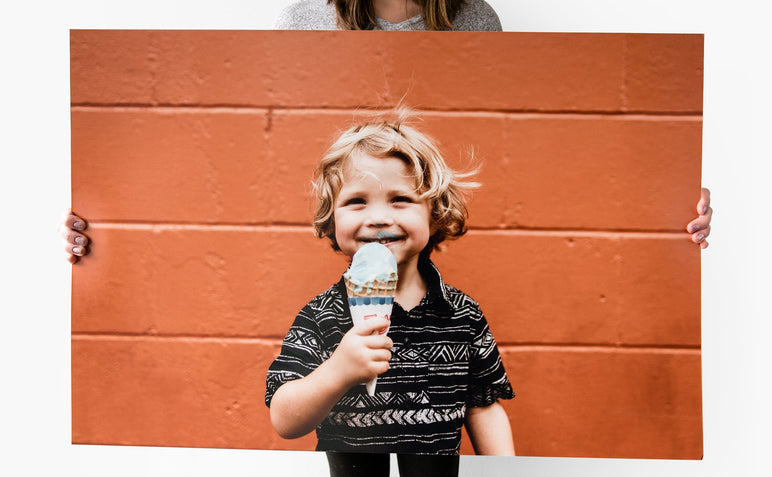 24x36" Photo Print being held up by a woman. The Photo Print features a picture of a young child eating ice cream in front of an orange wall.