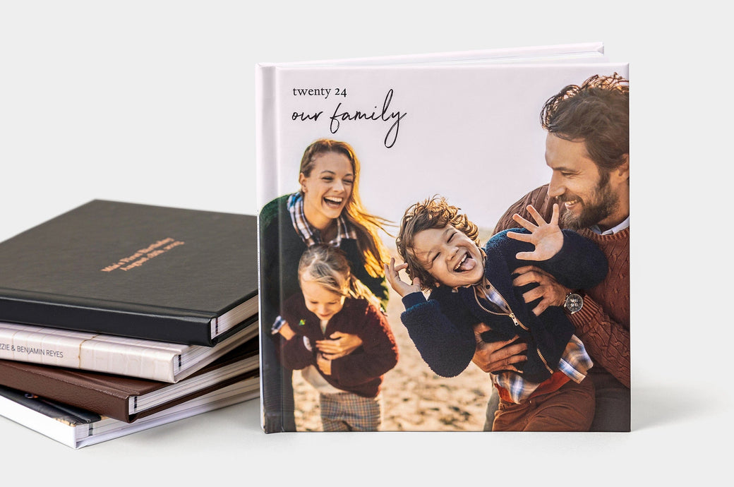 Four 8x8" Lay Flat Photo Books stacked on top of each other, one additional 8x8" Lay Flat Photo Books with a Photo Wrap Cover standing in front of the stack. 