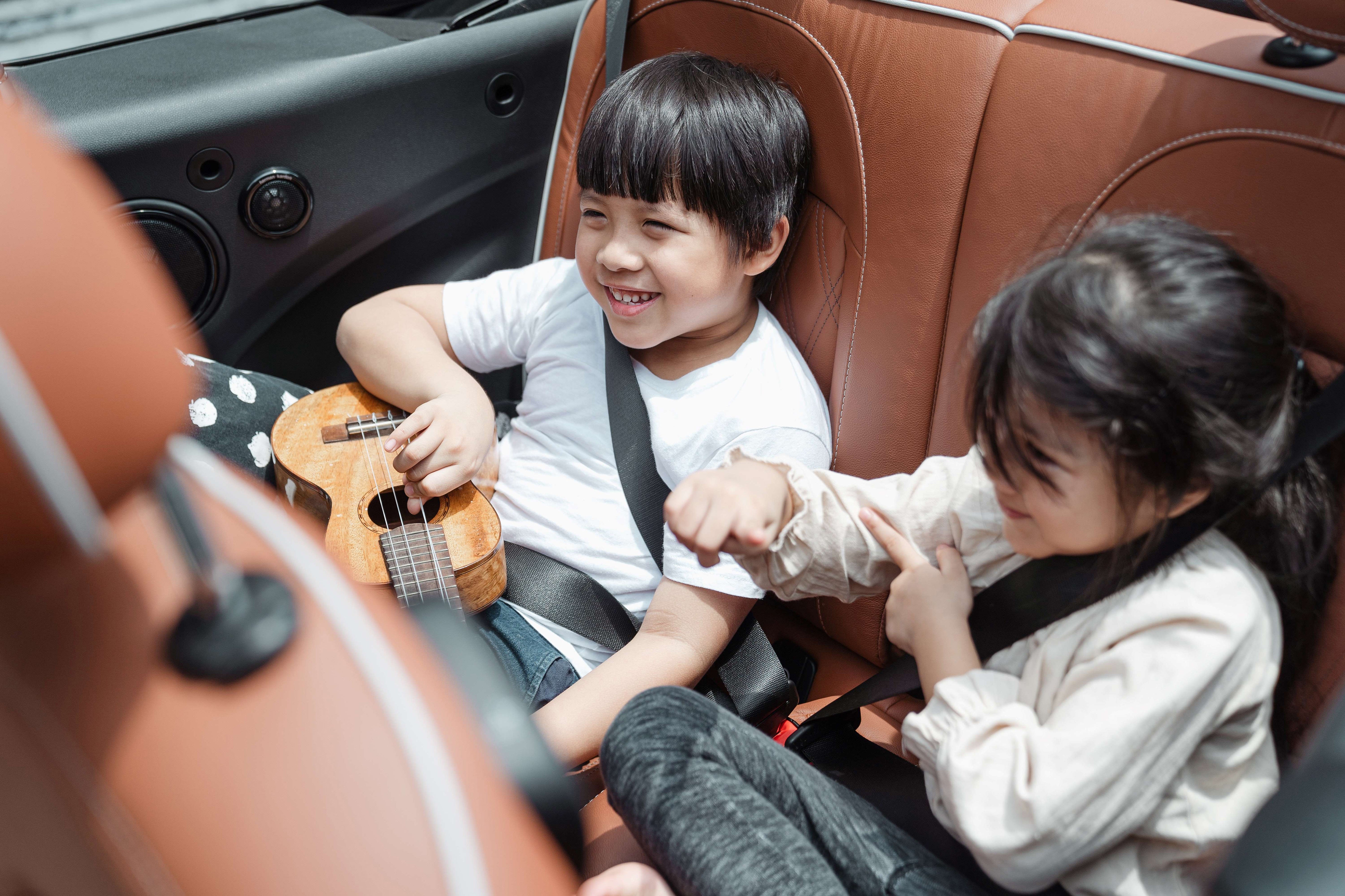 Image of two children in a backseat, one is holding a ukelele and both are laughing