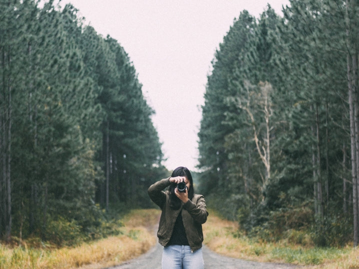 Female photographer stands in wooded path