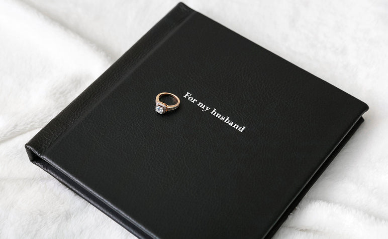 Overhead shot of a Boudoir Album99 cover with Black Leather and Silver Embossing that says "For my husband."