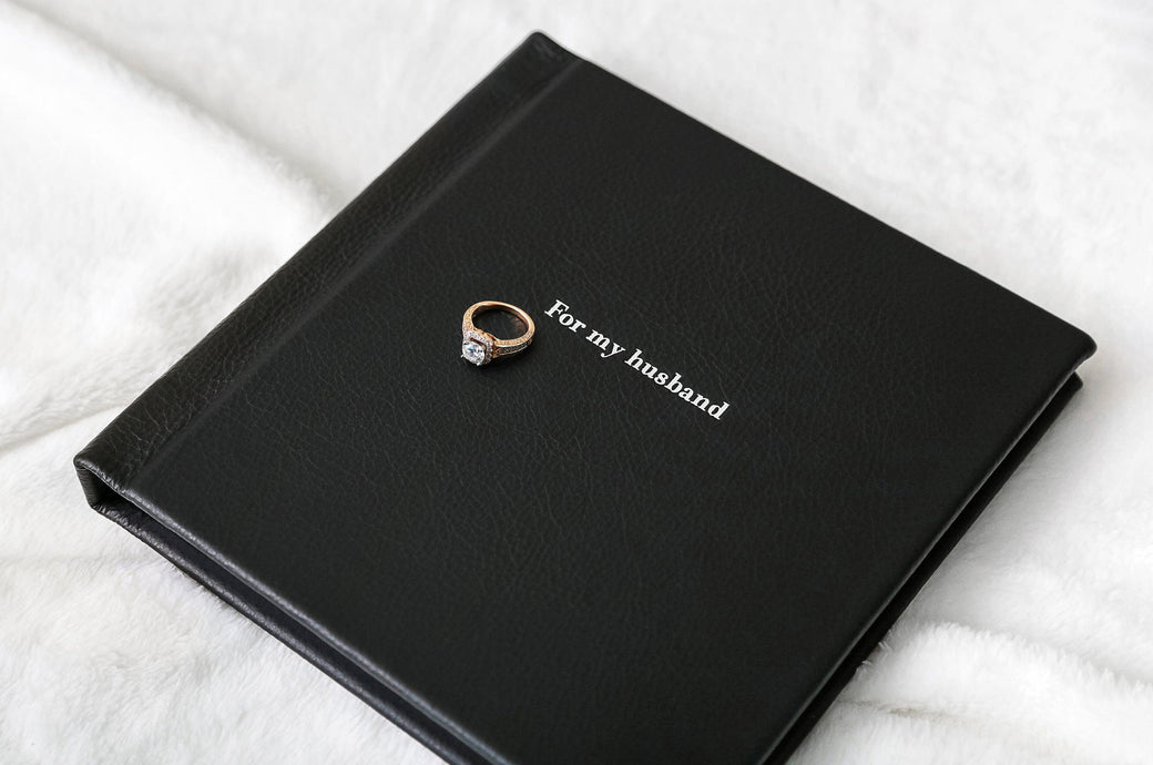 Overhead shot of a Boudoir Album99 cover with Black Leather and Silver Embossing that says "For my husband."