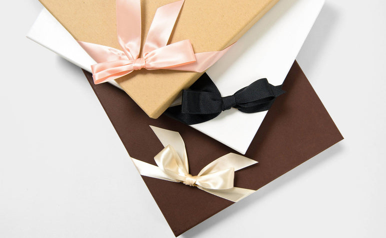 Three Boutique Boxes, one kraft with pink ribbon, one pebble with black ribbon, and one coffee with cream ribbon.