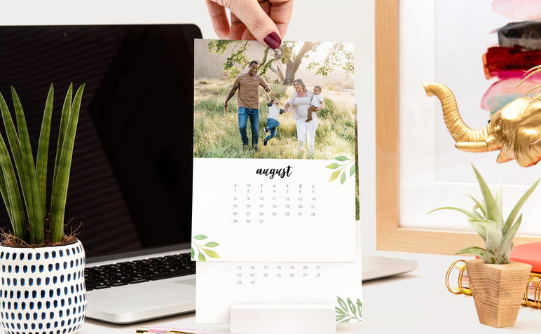 Woman's hand changing the month of her Desk Calendar, the top card has the month of August with a photo of a family. 