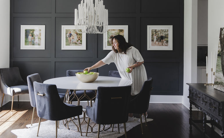 Dining room scene of a woman in front of a series of four 24x24" White Wood Framed Prints on a blue wall. 