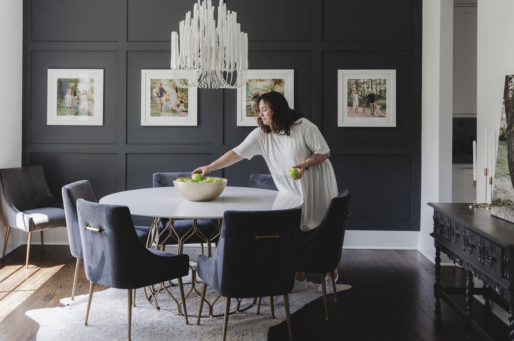 Dining room scene of a woman in front of a series of four 24x24" White Wood Framed Prints on a blue wall. 
