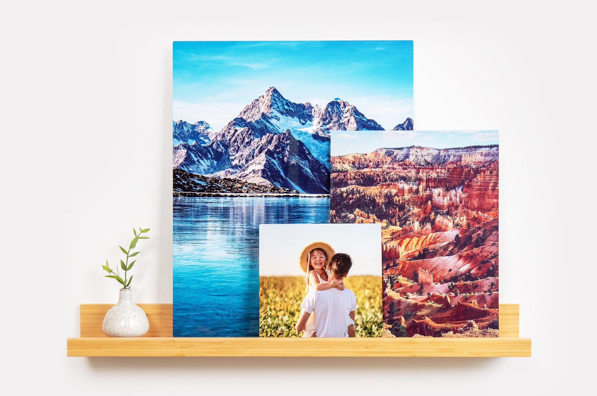 Three Metal Prints of different sizes arranged on a photo ledge. The first Metal Print features a picture of a father and daughter, and the other two are photos of landscapes.