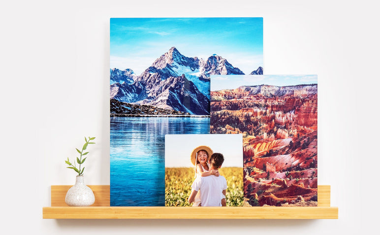 Three Metal Prints of different sizes arranged on a phtoo ledge. The first Metal Print features a picture of a father and daughter, and the other two are photos of landscapes. 