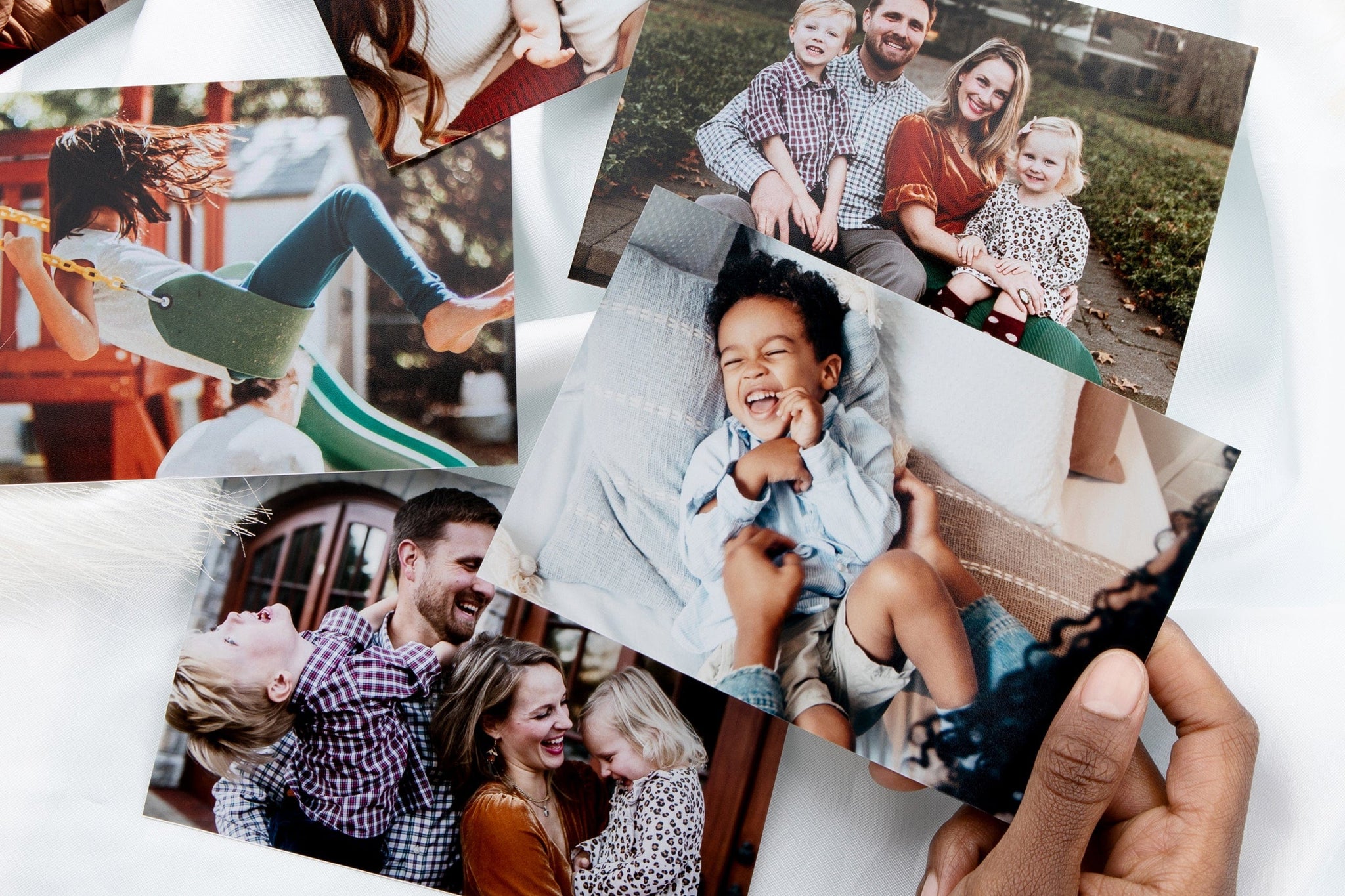 4x6" Photo Prints scattered on a white surface. The Prints feature families and child, one print with a laughing child is being held up by a woman's hand. 