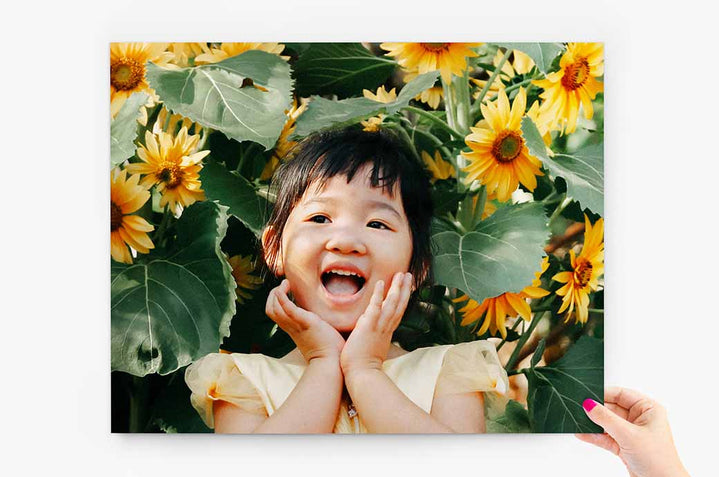11x14" Photo Print being held by a woman's hand. The Photo Print features a young child with sunflowers around her - Nations Photo Lab
