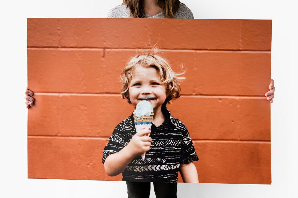 24x36" Photo Print being held up by a woman. The Photo Print features a picture of a young child eating ice cream in front of an orange wall.