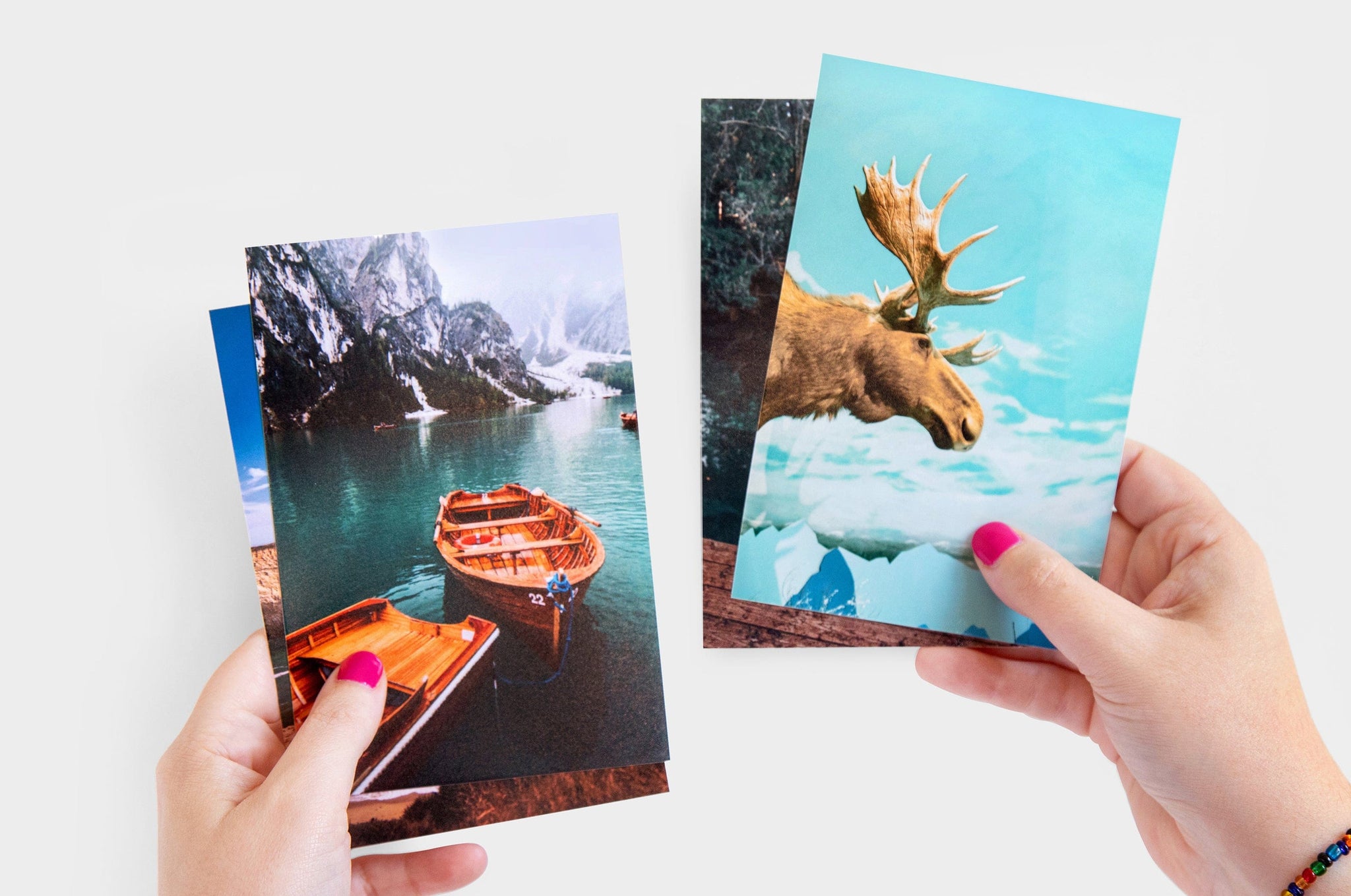 Woman's hands holding up several 4x6" Photo Prints, the top prints feature photos of a boat and a moose.